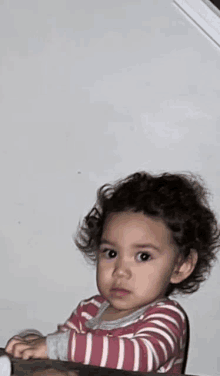 a little girl with curly hair is wearing a pink and white striped pajama set .