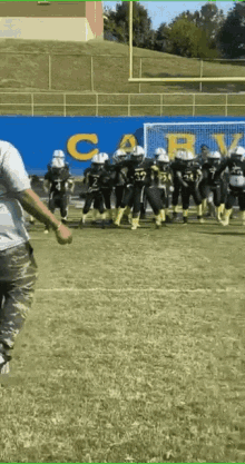 a group of young boys are playing football on a field with a blue wall behind them that says cary .