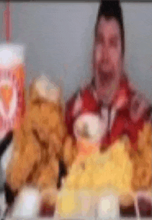 a blurry picture of a man sitting at a table eating chicken and french fries .