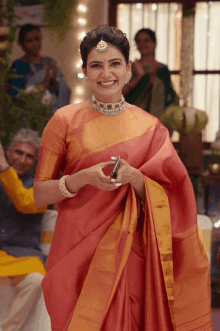 a woman in a red saree is smiling and holding a phone