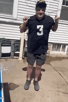 a man wearing a black jersey with the number 3 on it is standing in front of a white house .