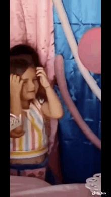 a little girl is sitting at a table with balloons and a pink curtain in the background .