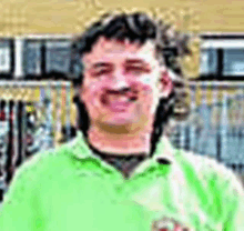 a man in a green shirt is smiling for the camera while standing in front of a building .