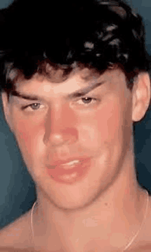 a close up of a young man 's face with red cheeks and a necklace around his neck .