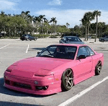 a pink car is parked in a parking lot next to a palm tree .