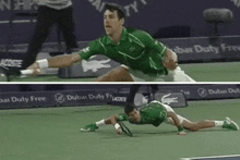 a man in a green shirt is stretching on a tennis court in front of a dubai duty free sign