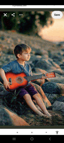 a young boy sits on a rock holding a guitar