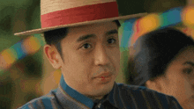 a man wearing a straw hat with a red ribbon looks at the camera