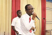 a man singing into a microphone in front of a red curtain