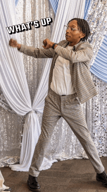 a man in a suit is dancing in front of a curtain that says what 's up on it