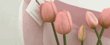 a bunch of pink tulips are sitting on a table next to a piece of paper .