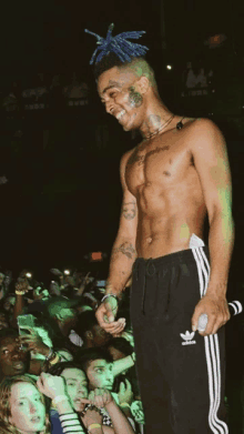 a shirtless man wearing black adidas sweatpants is standing in front of a crowd