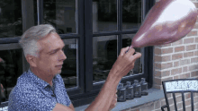 a man in a blue shirt is blowing up a balloon in front of a window