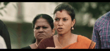 a woman in an orange saree is standing next to another woman in a plaid shirt .