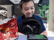 a boy sitting at a table with a bag of lays chips and a puma backpack