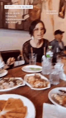 a woman is sitting at a table with plates of food and a sign that says nopparai cuisine and gallery