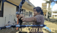 a girl is holding a bow and arrow in front of a building that says naga city archery on it