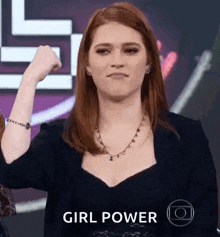 a woman with red hair is flexing her fist in front of a sign that says ' girl power ' .