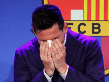 a man in a suit covering his face in front of a fcb logo