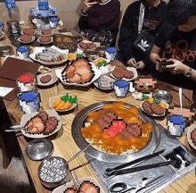 a group of people are sitting at a table with plates of food and a bowl of meat .