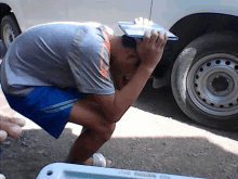 a man is kneeling down with his head in his hands in front of a white car with the word captain on the tire