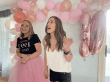 two women standing in front of balloons one wearing a black shirt that says limited