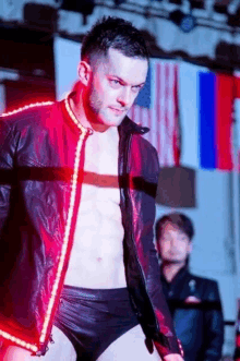 a man in a leather jacket and black underwear is standing in front of flags