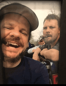 a man with a beard is smoking a cigar while another man looks on