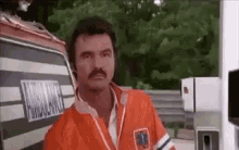 a man with a mustache is standing in front of an ambulance on a highway .