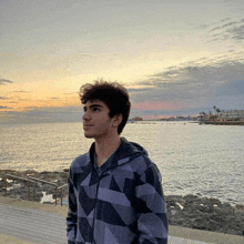 a young man in a plaid jacket stands in front of a body of water