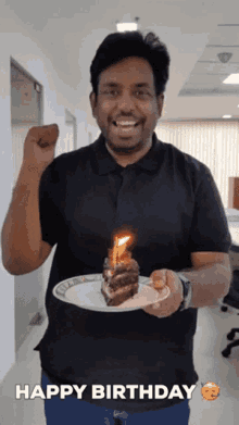 a man in a black shirt is holding a plate with a birthday cake on it and a candle lit up