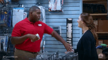 a man in a red shirt is talking to a woman in a store while holding a piece of paper .