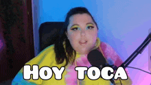 a woman sitting in front of a microphone with the words hoy toca written on her face