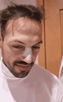 a man with a bandage on his nose is wearing a white shirt .