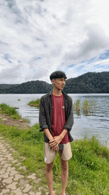 a young man standing in front of a lake wearing a red shirt that says the north face