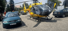 a yellow and black helicopter is parked next to a green audi car