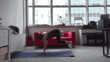 a woman is doing push ups on a yoga mat in front of a red couch with a sign that says rock n roll