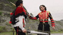 a man in a red and black uniform is holding a sword and talking to another man in a black and gold uniform