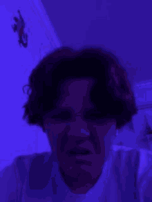 a person is making a funny face in a dark room with a purple light behind them .