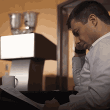 a man in a white shirt is writing on a piece of paper in front of a cup of coffee