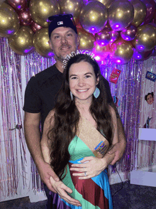 a man and a woman are posing for a picture with balloons in the background and a birthday girl sash