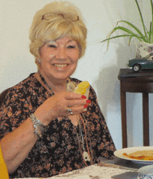 a woman sitting at a table with a plate of food and a drink in her hand