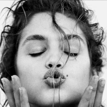 a black and white photo of a woman making a kiss with her eyes closed