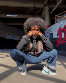 a person squatting in front of a wall with graffiti on it