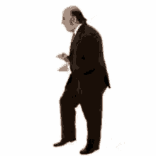 a bald man in a suit is walking across a white background .