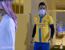 a man wearing a mask and a yellow etihad shirt