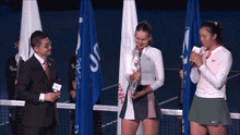 a man in a suit stands next to a woman holding a trophy and a woman in a nike skirt