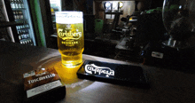 a glass of carlsberg beer sits next to a pack of toscanello cigarettes