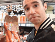 a man in a black jacket is holding a bag of carrots in front of a shelf with bottles of orange juice