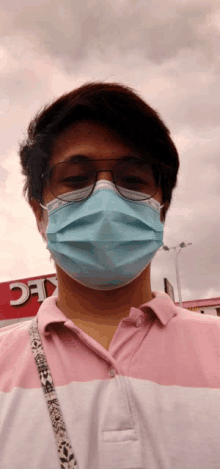 a man wearing a mask and glasses stands in front of a kfc sign